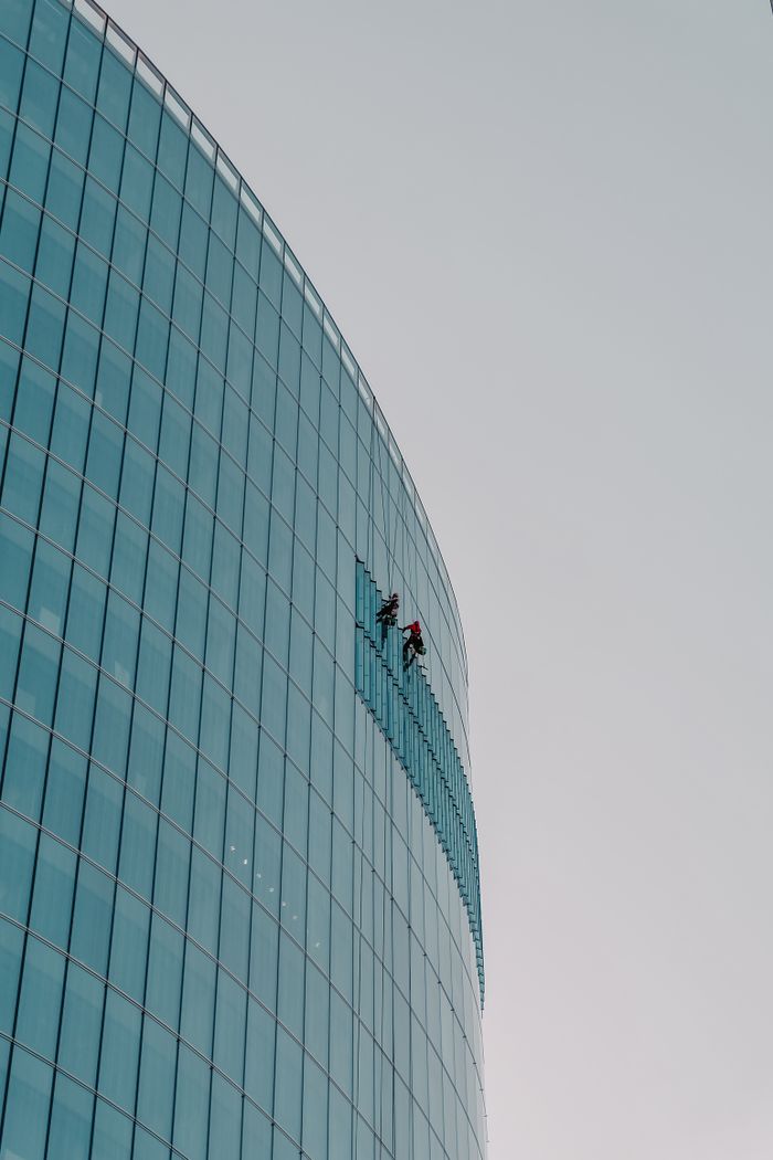 High-rise window cleaners scaling a curved glass skyscraper facade in daylight.