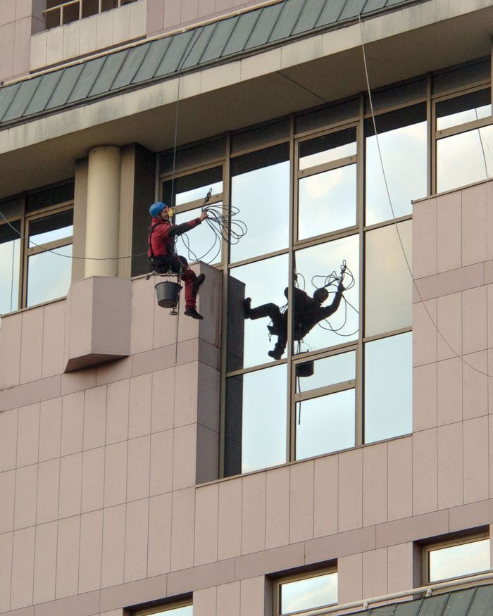 Two professional window cleaners working on a skyscraper, ensuring safety with harnesses.